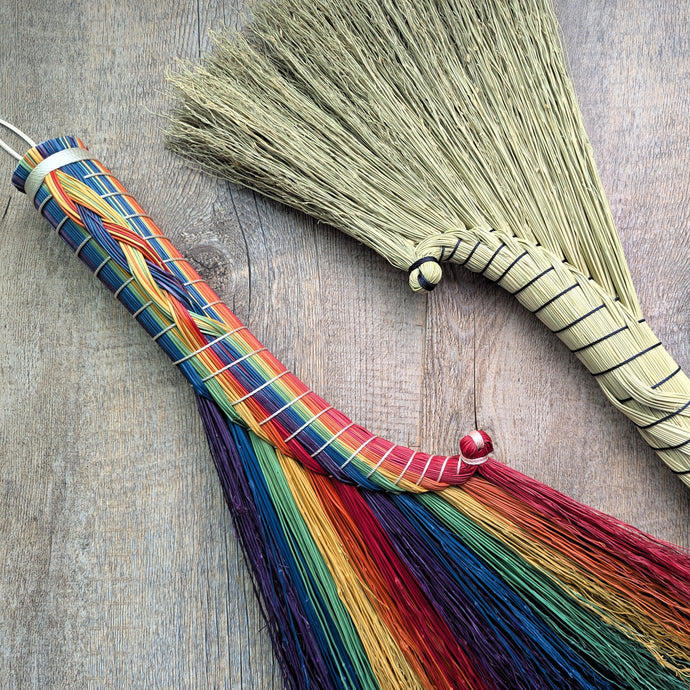 Broom with rainbow bristles and a broomstick handle on a wooden surface