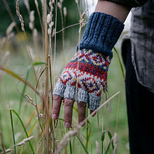 Hand wearing a colorful knitted glove in a natural setting with tall grass.
